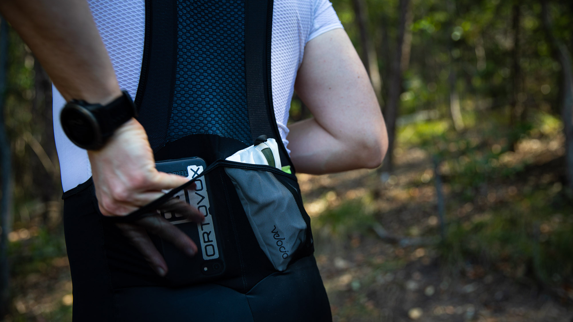 Male cyclist wearing some of the best cargo bib shorts, placing his phone in to a rear pocket.